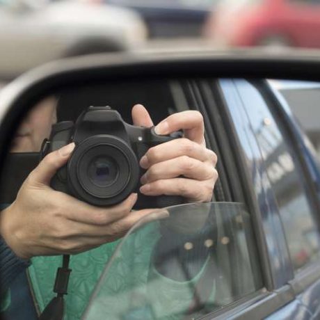 Hidden photographing. Reflection in car mirror of a private detective with camera.